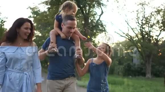 夫妻和他们的孩子一起散步一个小女孩坐在她父亲的肩膀上快乐的家庭假期视频的预览图