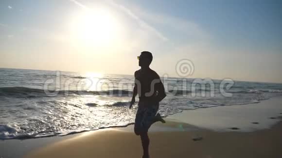 日出时年轻运动男子沿着海岸快速奔跑的剪影在海边训练运动男孩男性视频的预览图