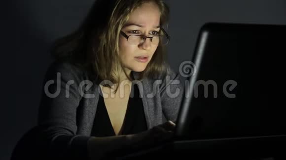 戴眼镜的女人在黑暗的房间里用电脑看着显示器开始沮丧视频的预览图