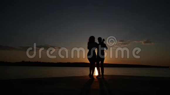 小男孩和小女孩在湖边日落时跳舞剪影拍摄慢动作视频的预览图