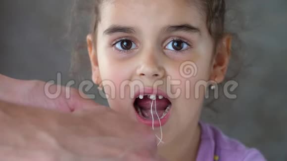 大人的手把绑在孩子牙齿上线拉成功地尝试移除牙齿拉出来视频的预览图