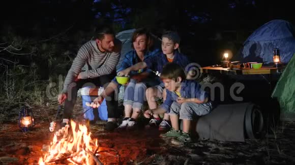 父母带着孩子在篝火上烤棉花糖到林地幸福的家庭在大火中煎棉花糖视频的预览图
