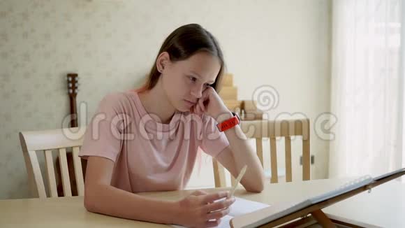 可爱的少女看着一本书写在笔记本上然后看着她的手表家庭教育的概念后格里客厅视频的预览图