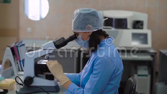 女医学研究助理穿蓝色实验服在实验室工作在显微镜下检查样品视频的预览图