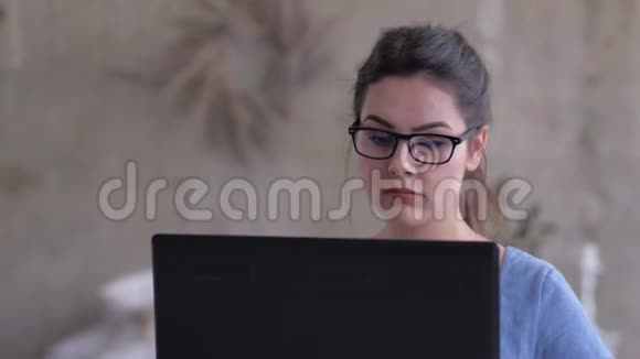 戴眼镜的自由职业者女孩在笔记本电脑上工作的肖像坐在家里特写视频的预览图