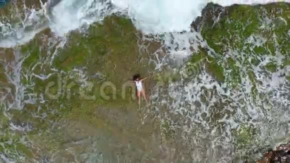 空气视图海浪溅起泡沫喷向石质海岸美丽的女人躺在岩石海滩上视频的预览图
