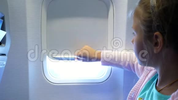特写镜头小女孩举起舷窗窗帘在飞机的机舱里从那里发出明亮的光一个女孩视频的预览图