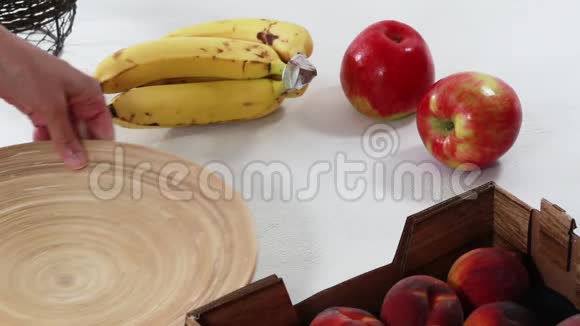 木制盘子上的水果苹果香蕉和桃子贴在白色背景上女人的手视频的预览图
