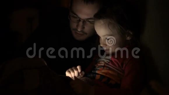 小女孩和爸爸在黑暗的房间里玩手机游戏视频的预览图
