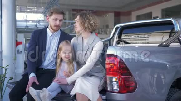 汽车沙龙带孩子的年轻家庭选择汽车坐在汽车后备箱交流视频的预览图