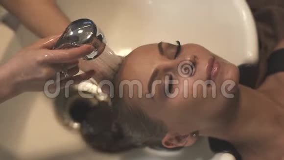在美发沙龙用洗发水洗头时面对美丽的女人年轻女子在美女面前洗头视频的预览图