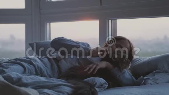 美丽浪漫的黑发女人躺在床上和缅因州的猫在窗边睡觉视频的预览图