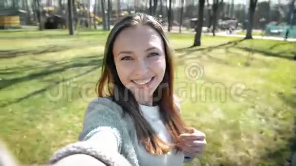 一幅美丽的年轻女人用智能手机在公园自拍的肖像视频的预览图