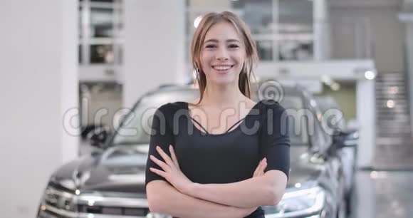 快乐的白人女孩在模糊的黑色汽车背景下摆姿势年轻的微笑女人买车或在车里视频的预览图