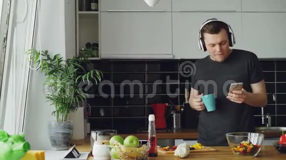 快乐的男人在厨房里跳舞唱歌早上在家里的智能手机上浏览社交媒体视频的预览图