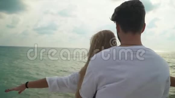 一对年轻的夫妇穿着白色的衣服站在海滩上男人从背后搂着女人女人举手视频的预览图