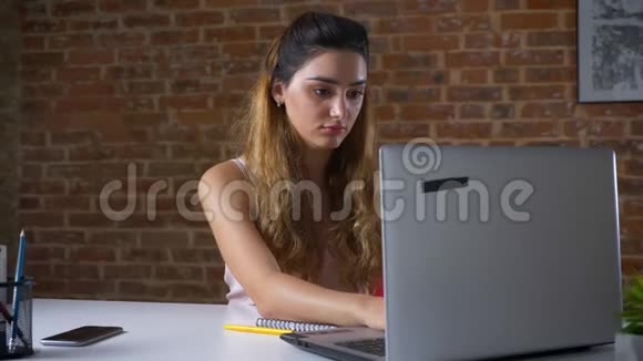 一位名叫妮丝的白种人的女性正在键盘上打字她用笔记本电脑突然停下来接电话办公室里有一间砖房视频的预览图