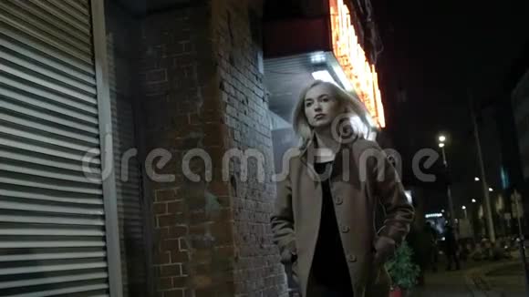 美丽的金发女人穿着外套晚上独自在户外散步谷物慢动作视频的预览图