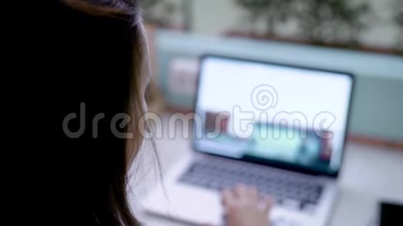 年轻的黑发女人正在浏览网站用笔记本上网购物在家里的透明房间里喝咖啡视频的预览图