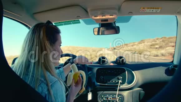 漂亮的金发女人吃香蕉作为男人的象征坐在司机的座位上抱着车视频的预览图