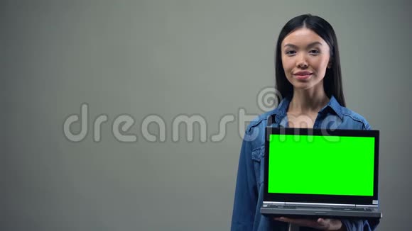微笑的女人竖起大拇指手持绿色屏幕笔记本电脑在线教育视频的预览图