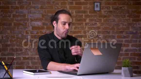 漂亮的白种人上班族在电脑前思考和咬手电脑后面有砖墙视频的预览图