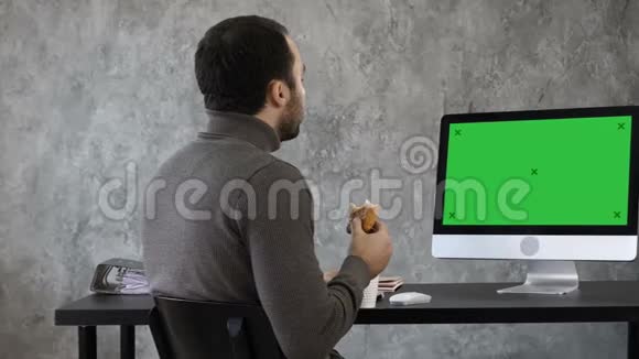 办公室里的商人在吃早餐午餐在Mac电脑上看东西绿色屏幕模拟视频的预览图