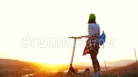 带着电动滑板车的女孩背着她站着看着夕阳慢悠悠地视频的预览图