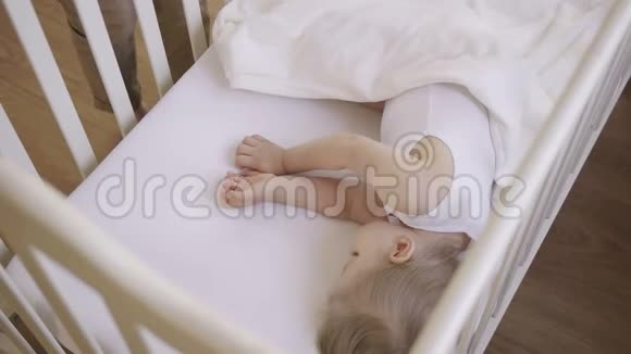 两岁的小女孩睡在铺着白色毯子的婴儿床上妈妈给宝宝盖上毯子日间睡眠视频的预览图