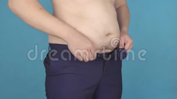 肥胖的年轻人大肚子的紧身裤腰部超重和肥胖的概念蓝色背景视频的预览图