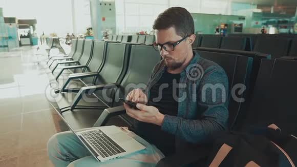 男性乘客坐在机场候车厅通过智能手机发送短信视频的预览图