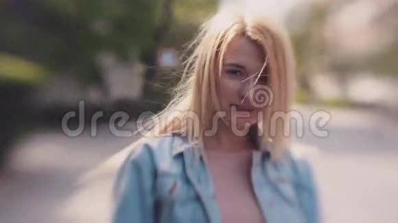 年轻的金发美女穿着牛仔裤夹克在街上闲逛刮风的天气秃发可爱的微笑视频的预览图