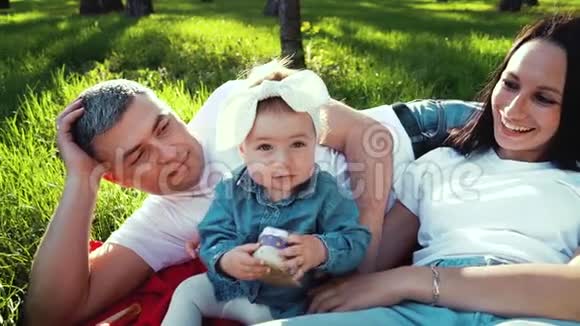 可爱的女婴抱着鞋子父母躺在公园的草地上视频的预览图