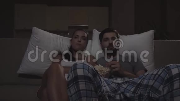男人和女人坐在沙发上看电影他们吃爆米花女孩开始睡着了他们看起来视频的预览图