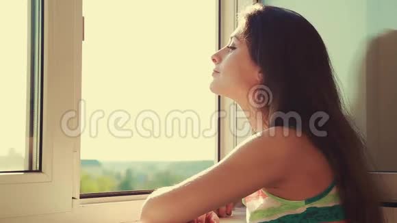 想着年轻的女人从窗外看享受空气视频的预览图