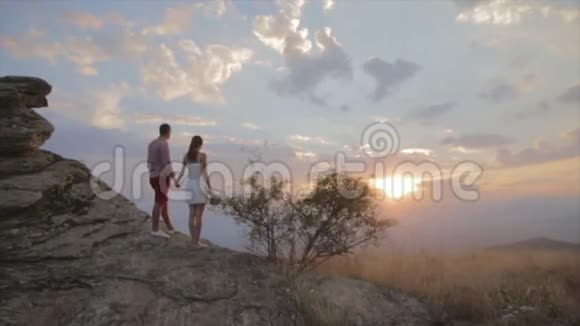 一对夫妇站在岩石上看山顶上的日落视频的预览图