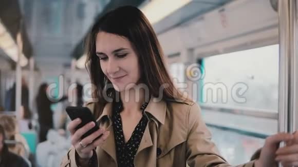 高加索女人在地铁里用智能手机美丽幸福青年上班族从手机APP上阅读新闻5G4K视频的预览图