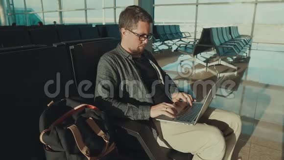 独自一人的男乘客在候机楼等候在笔记本电脑上浏览视频的预览图