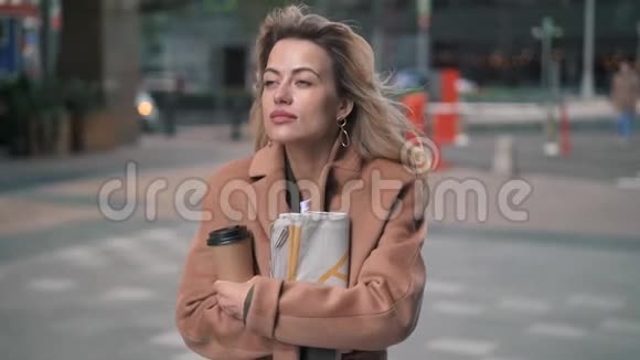 金发女人带着咖啡在秋天的街道上冻得发抖视频的预览图