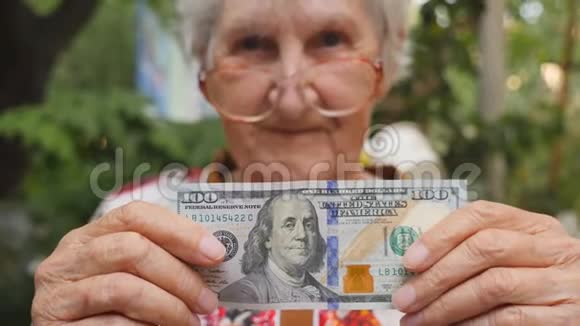 戴着眼镜的老妇人把100美元的钞票放进室外摄像机里快乐奶奶持有外币视频的预览图