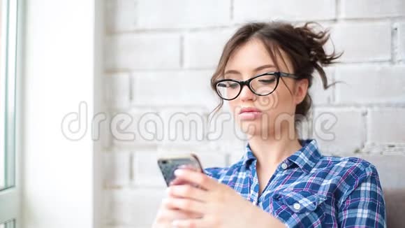 漂亮的年轻女人用智能手机微笑在室内快乐女孩短信短信使用应用程序智能手机在家里视频的预览图
