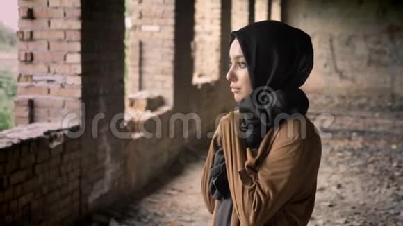 年轻漂亮的穆斯林妇女戴着黑色头巾站在废弃的大楼里惊恐地看着摄像机视频的预览图