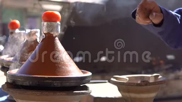 传统的摩洛哥塔吉因食品烹饪在塔吉因锅上的火与烟雾和西红柿顶部本地厨师手视频的预览图