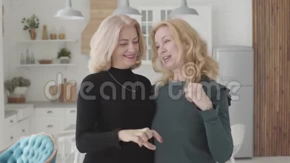 微笑着成熟的高加索女人站在豪华的厨房里手指颤抖成心形富有的资深女性视频的预览图
