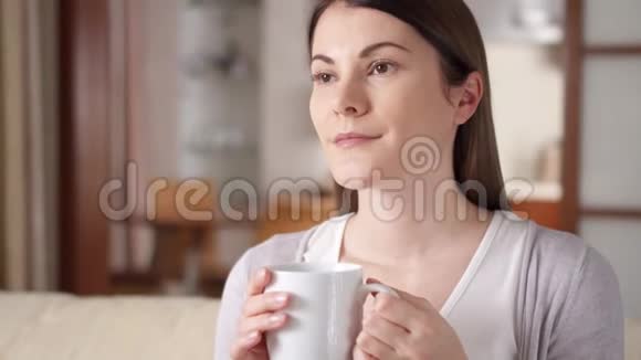 年轻女子在家里的沙发上放松漂亮的女性在客厅喝咖啡或茶视频的预览图