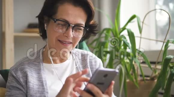 戴眼镜和耳机滚动屏幕的成熟女性视频的预览图