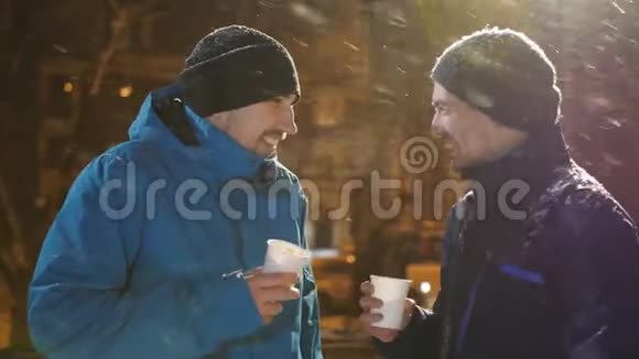 冬天的晚上两个男人在街上聊天喝咖啡下雪了视频的预览图