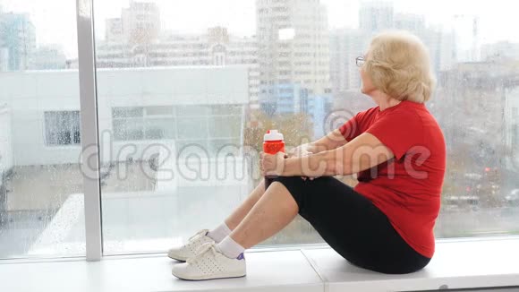 积极主动的老年妇女坐在健身房的窗台上训练后休息背景全景窗视频的预览图