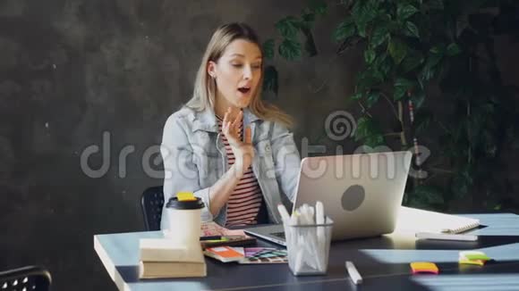 有魅力的年轻女性正在电脑上通过Skype聊天而坐在现代办公室的桌子上她在说话视频的预览图