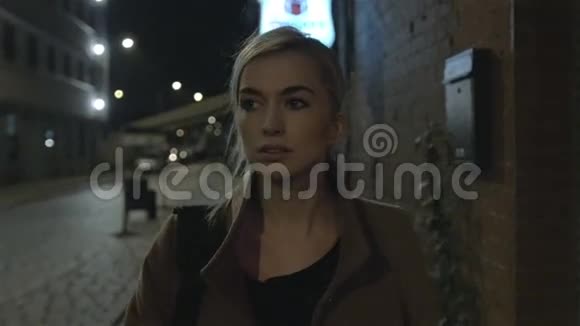 美丽的金发女人穿着外套晚上独自在户外散步谷物慢动作视频的预览图